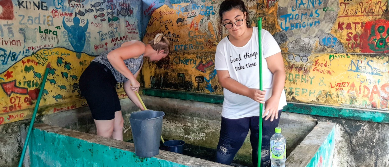 Two women clean a large tank at a turtle conservation center with graffiti walls in Ambalangoda, Sri Lanka.